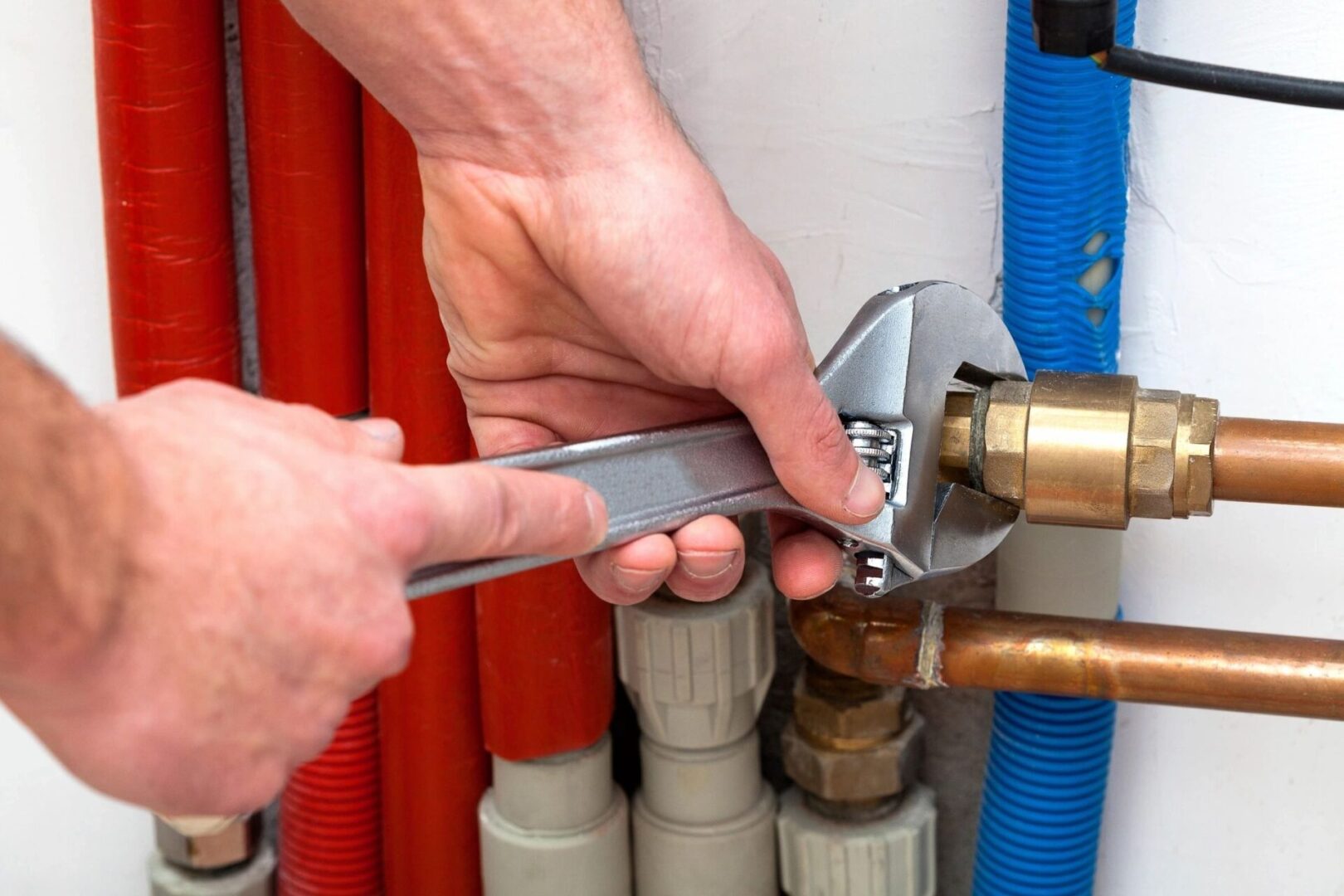 A person holding a wrench over pipes and valves.